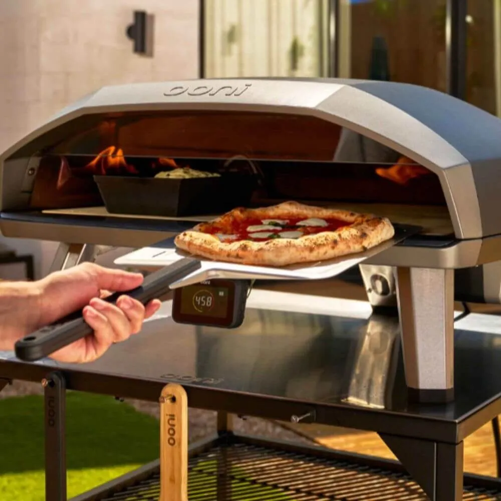 Ooni Koda 2 Max gas pizza oven cooking a fresh pizza with peel, dual-burner flame visible and digital temperature display