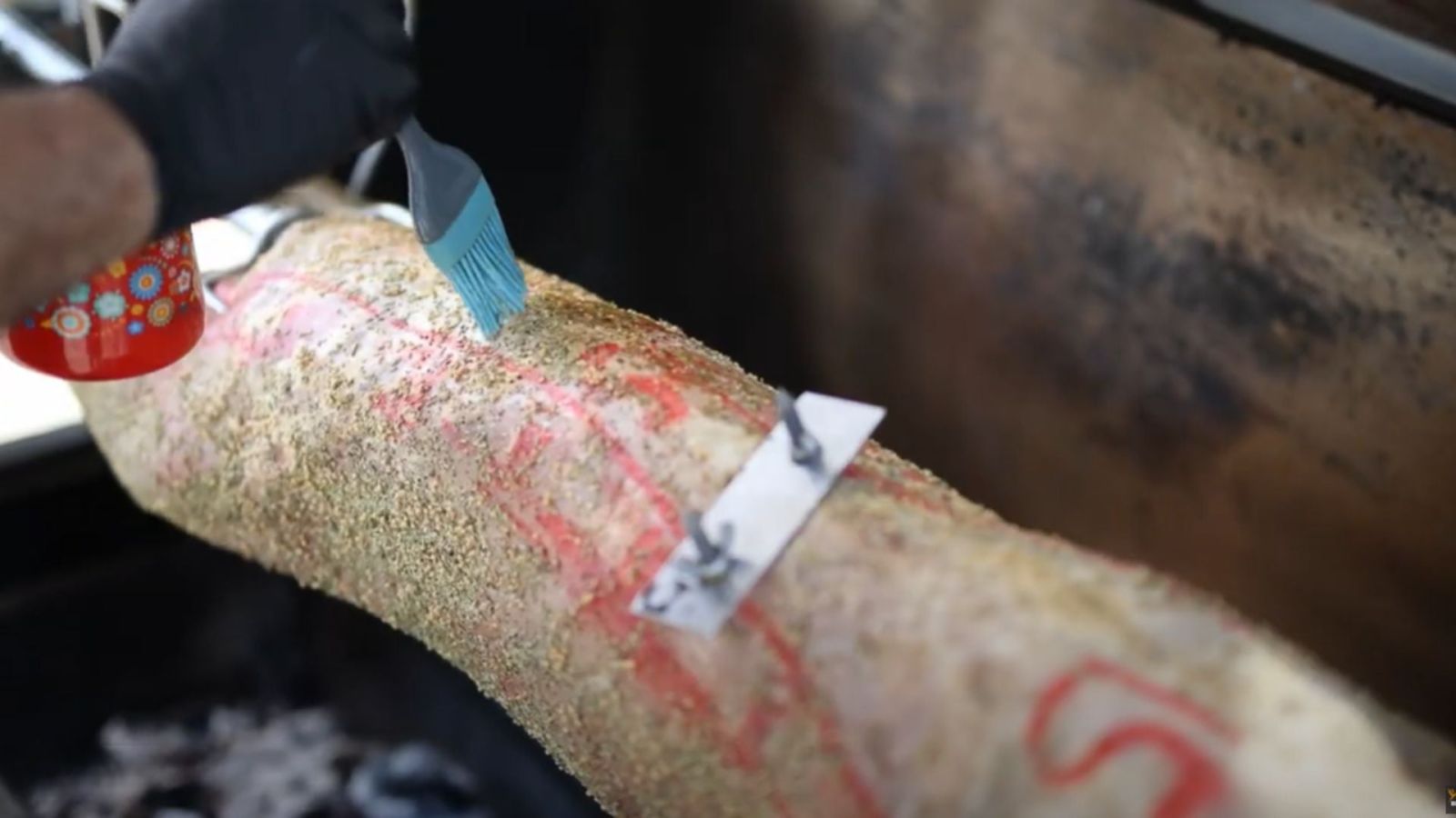 Basting whole lamb on spit roaster – marinade brushed onto rotisserie lamb for flavour