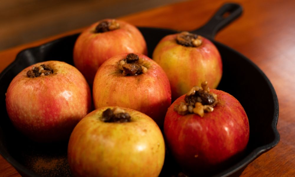 Cored apples stuffed with a mixture of walnuts, raisins, and honey, arranged in a cast iron skillet ready for baking.