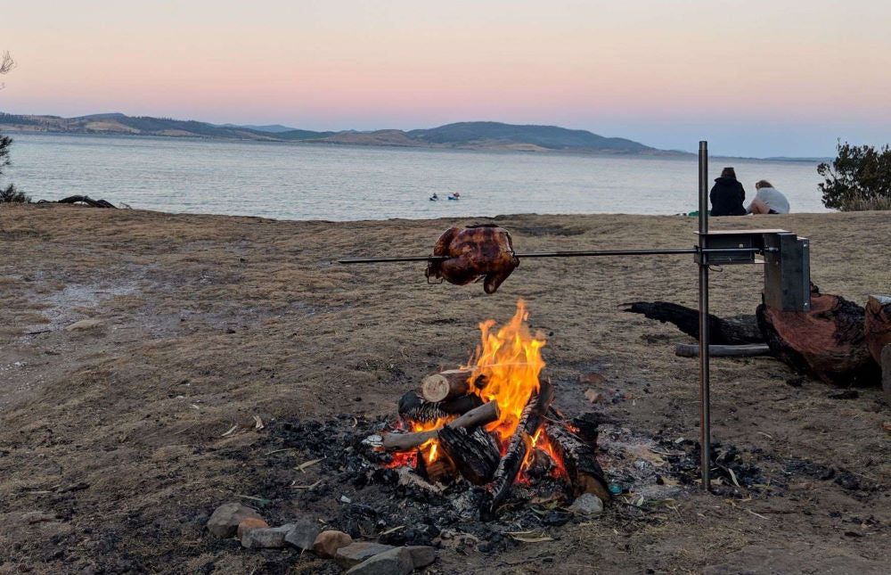 Roasting a whole chicken over an open campfire on a beach