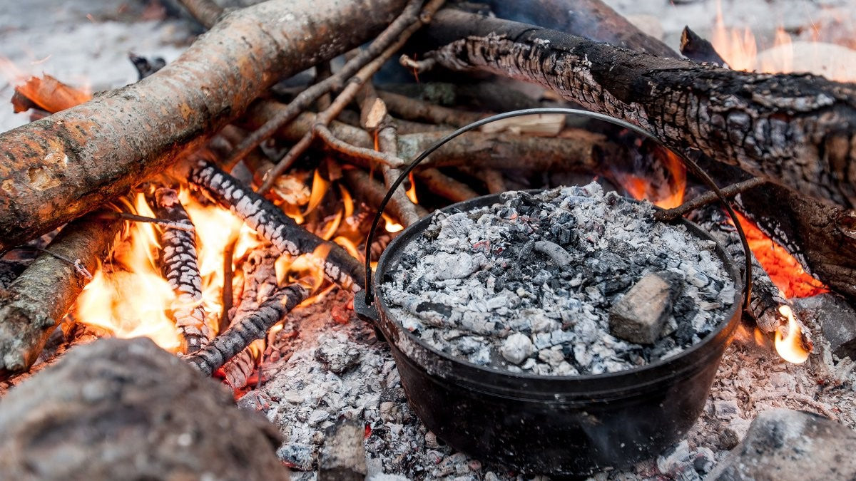 This is a picture of a cast iron camp oven cooking in front of a hot campfire