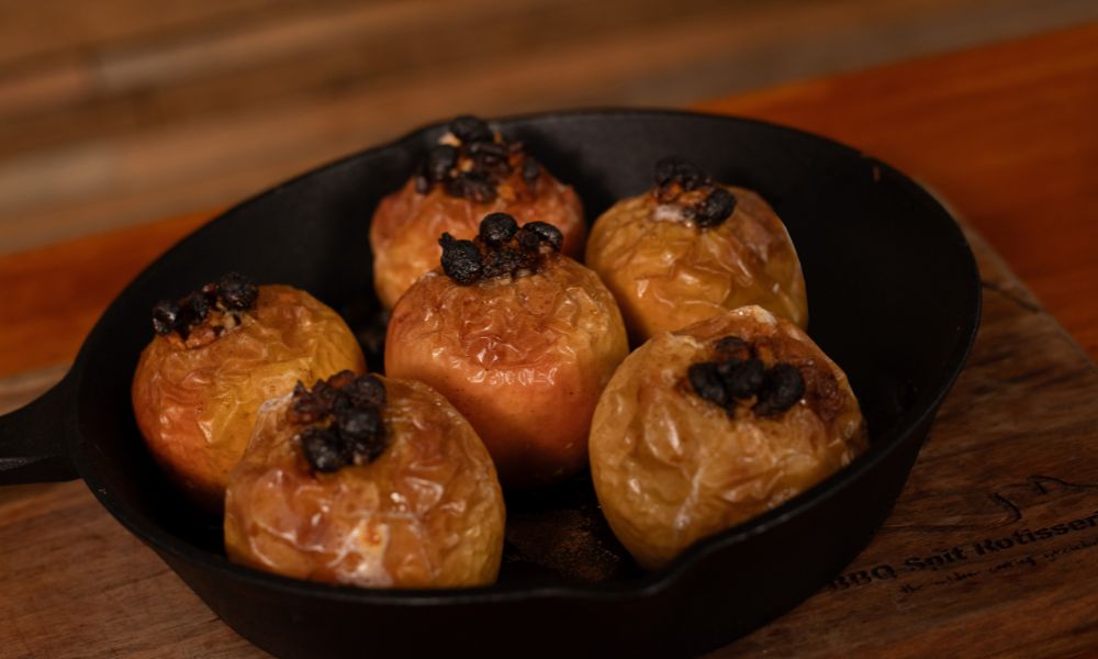 Freshly baked apples stuffed with raisins and nuts, caramelised and golden, served in a cast iron skillet on a wooden board.