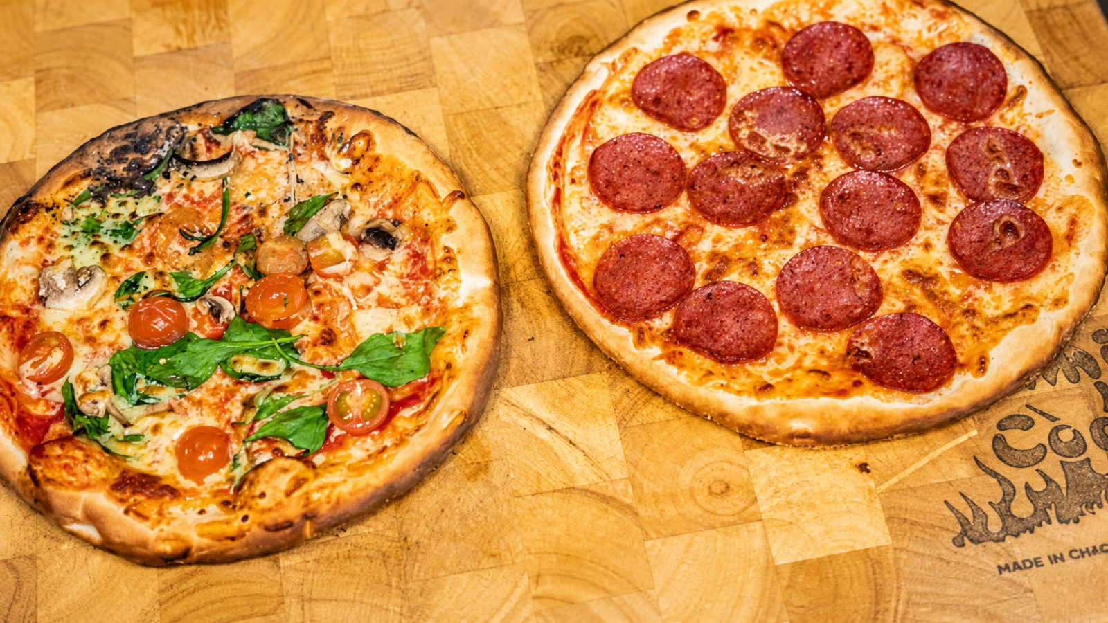 Vegetable and pepperoni pizzas with melted cheese on a wooden serving board.