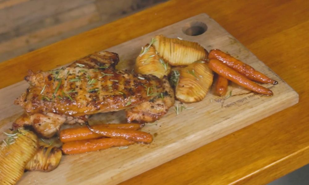 Grilled turkey pieces served with hasselback potatoes and roasted carrots on a wooden board.