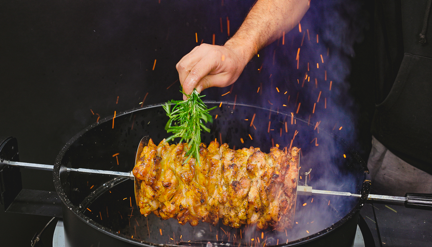 This image shows a man basting the gyro with olive oil and jemon using the rosemary