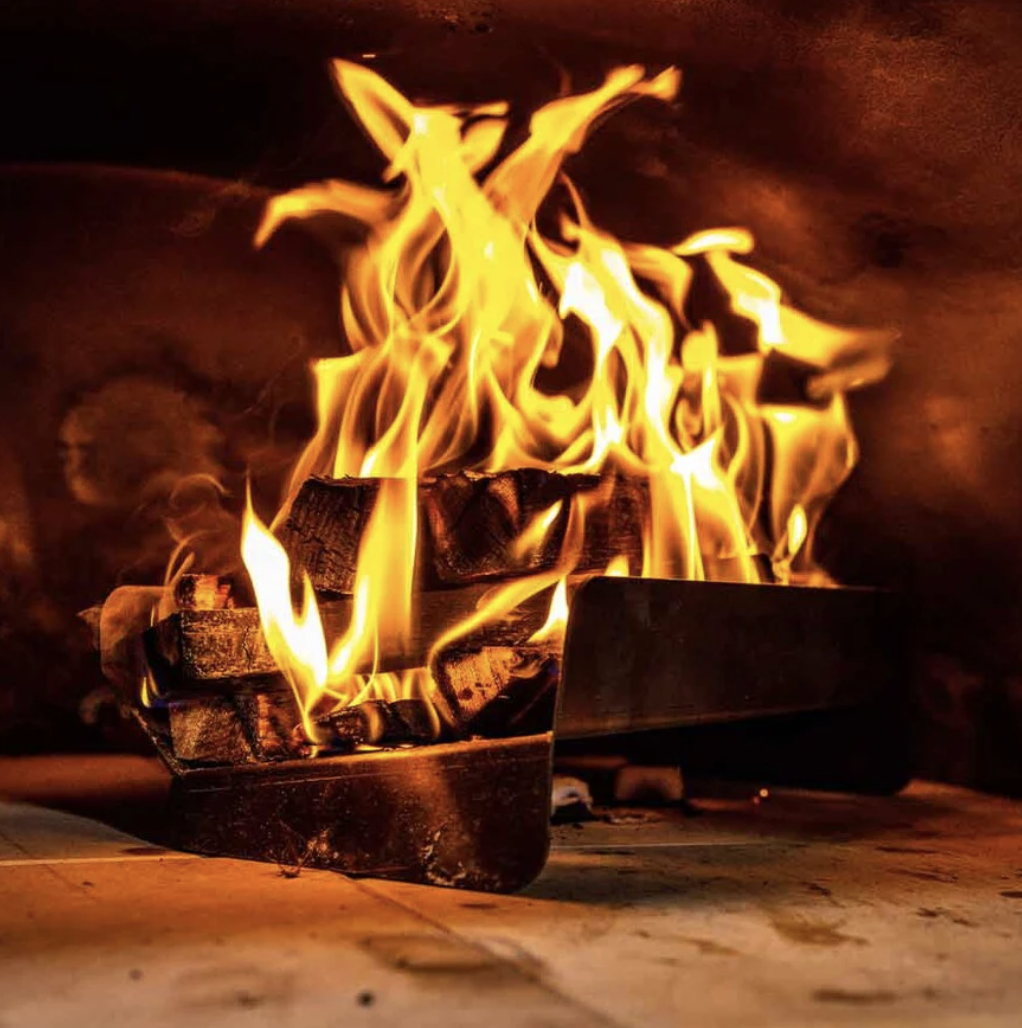 Hot burning fire inside a pizza oven. The fire is lit in a raised log holder that assist in higher temperature in the oven