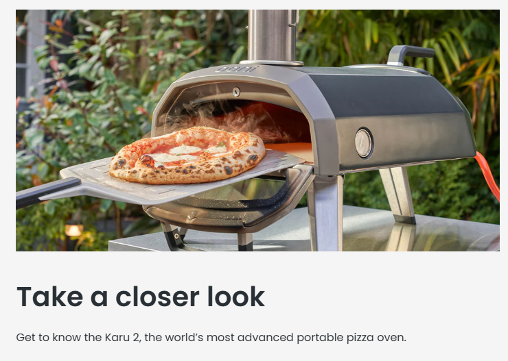 A freshly baked pizza being pulled out of the Ooni Karu 2 Multi-Fuel Pizza Oven using a metal pizza peel. The oven sits outdoors on a stainless steel table, surrounded by greenery, showcasing its sleek, portable design and high heat performance.