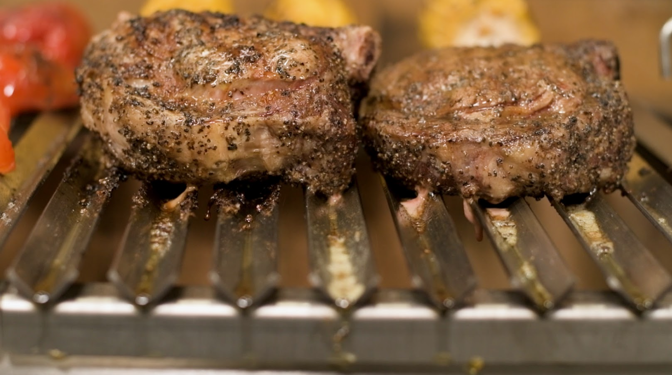 Close up of steaks searing on stainless steel V channel parrilla grill bars over live charcoal fire, showing V Channel Grills That Actually Work.