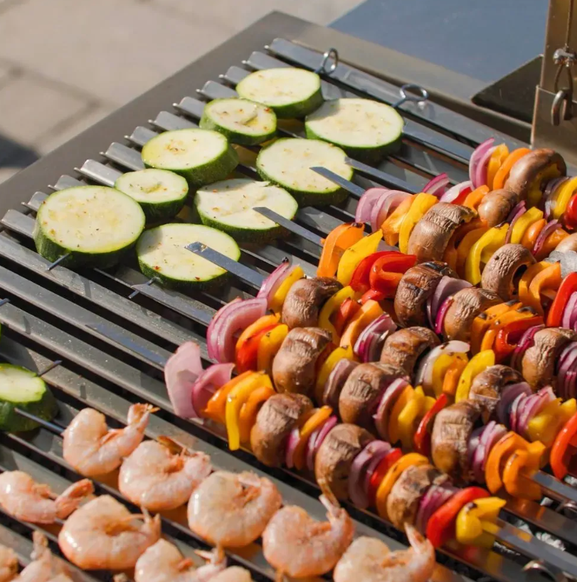 Vegetables and prawns cooking on stainless steel V channel parrilla grill grates.
