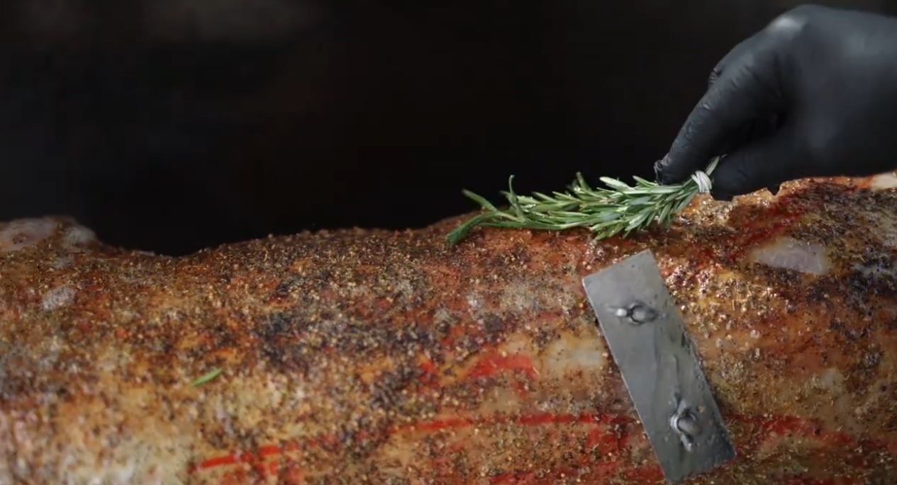 Basting whole lamb on spit roast with herbs during cooking