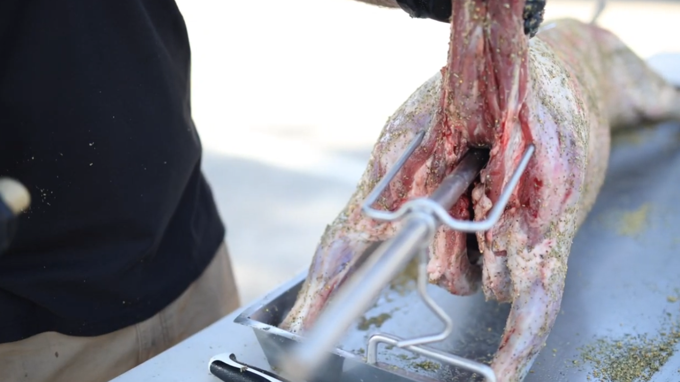 Securing whole lamb to spit rotisserie using leg bracket
