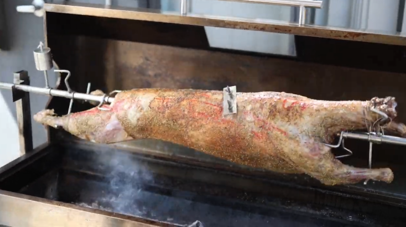 Whole lamb cooking on spit rotisserie over lump charcoal
