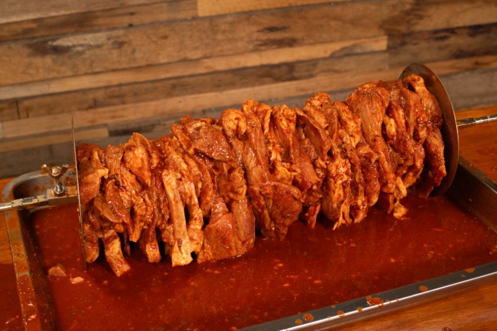 Marinated pork slices stacked tightly onto a spit skewer between gyros discs, ready for grilling al pastor style.