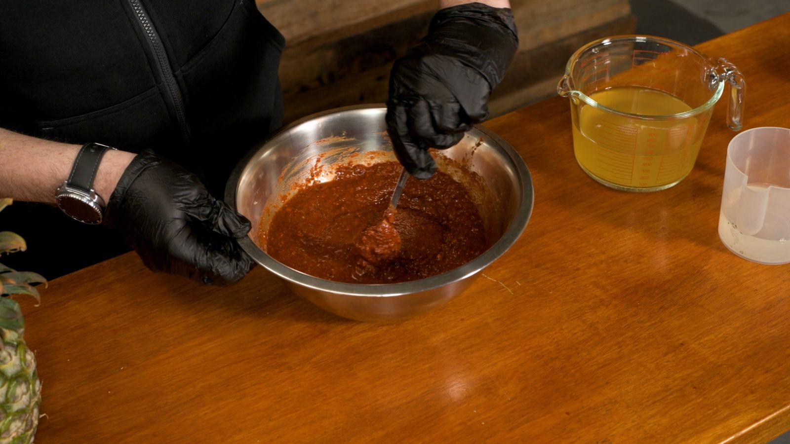 Preparing Al Pastor marinade by combining pineapple juice, vinegar, achiote paste, chipotle in adobo, cumin, paprika, herbs, salt, and pepper into a smooth paste for marinating pork.