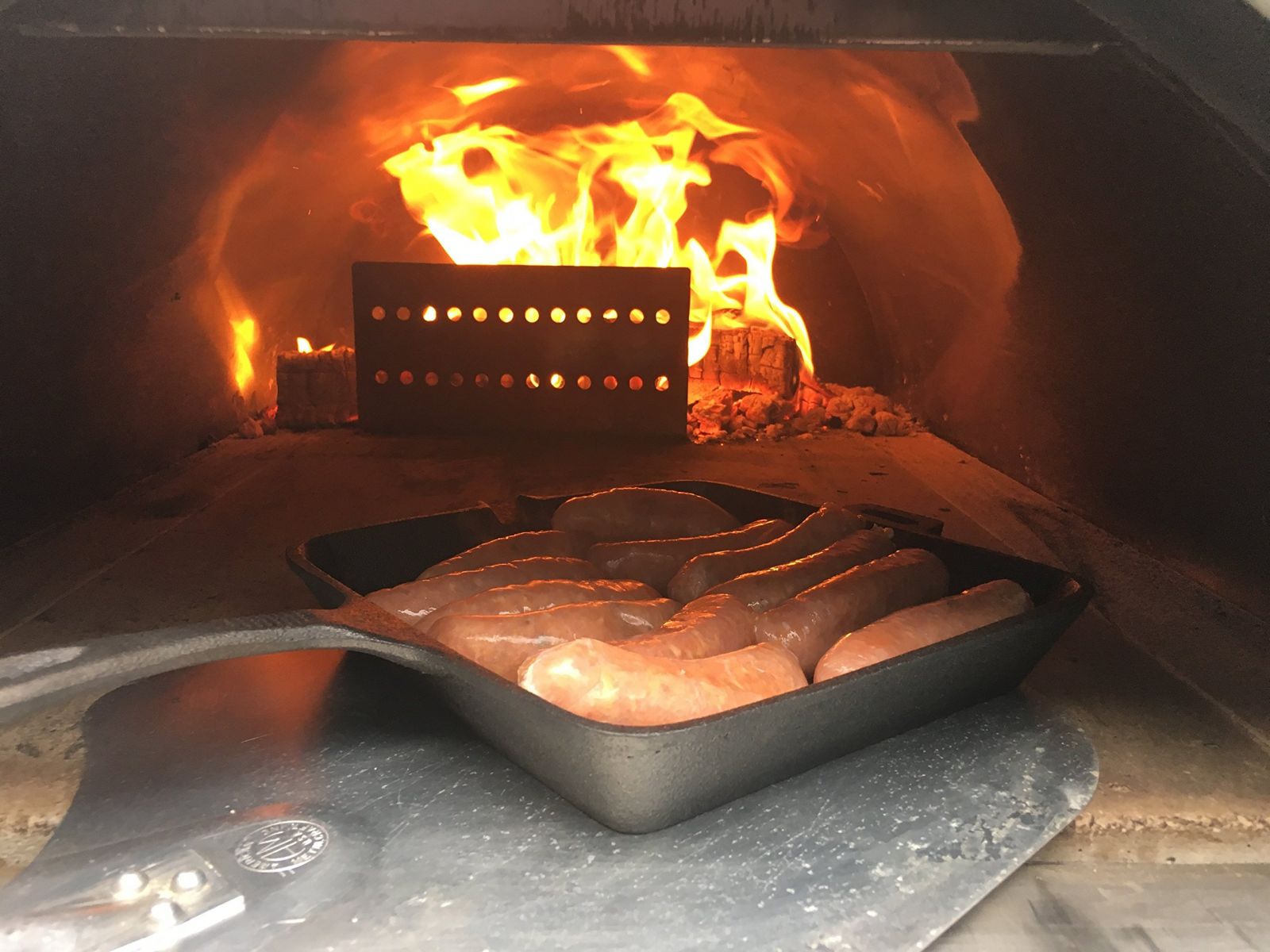 This image shows a burning fire in a pizza oven that is help back by a Stainless Steel Log Holder Flame Shield