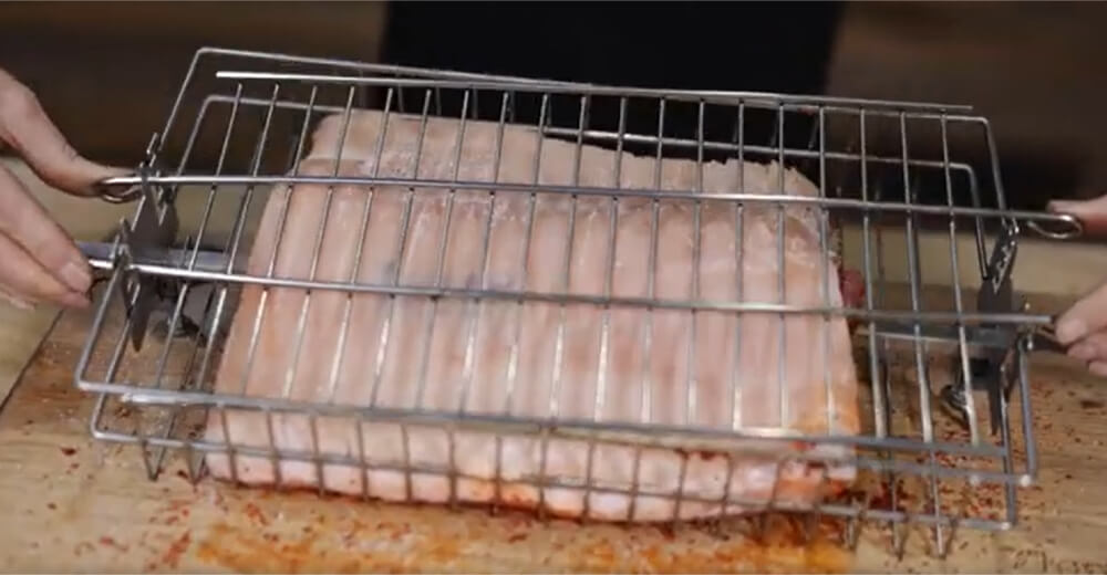 This image shows a pork belly being placed in the rotisserie basket