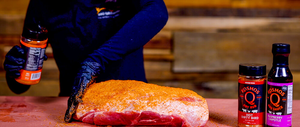 This image shows the pork shoulder being seasoned with Kosmos Q Rubs