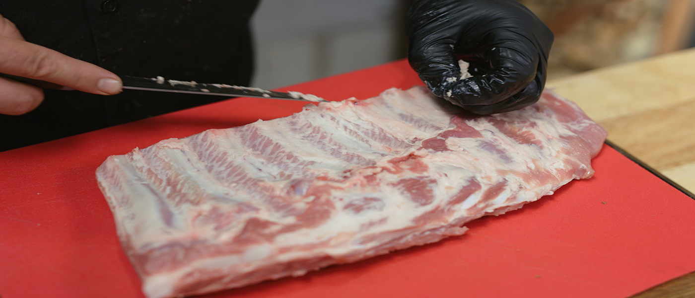This image shows a man removing the excess fat of pork ribs