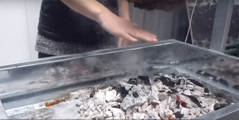 This picture shows the cook using their hand to determine the best height to have the meat above the charcoal on a spit roast. 