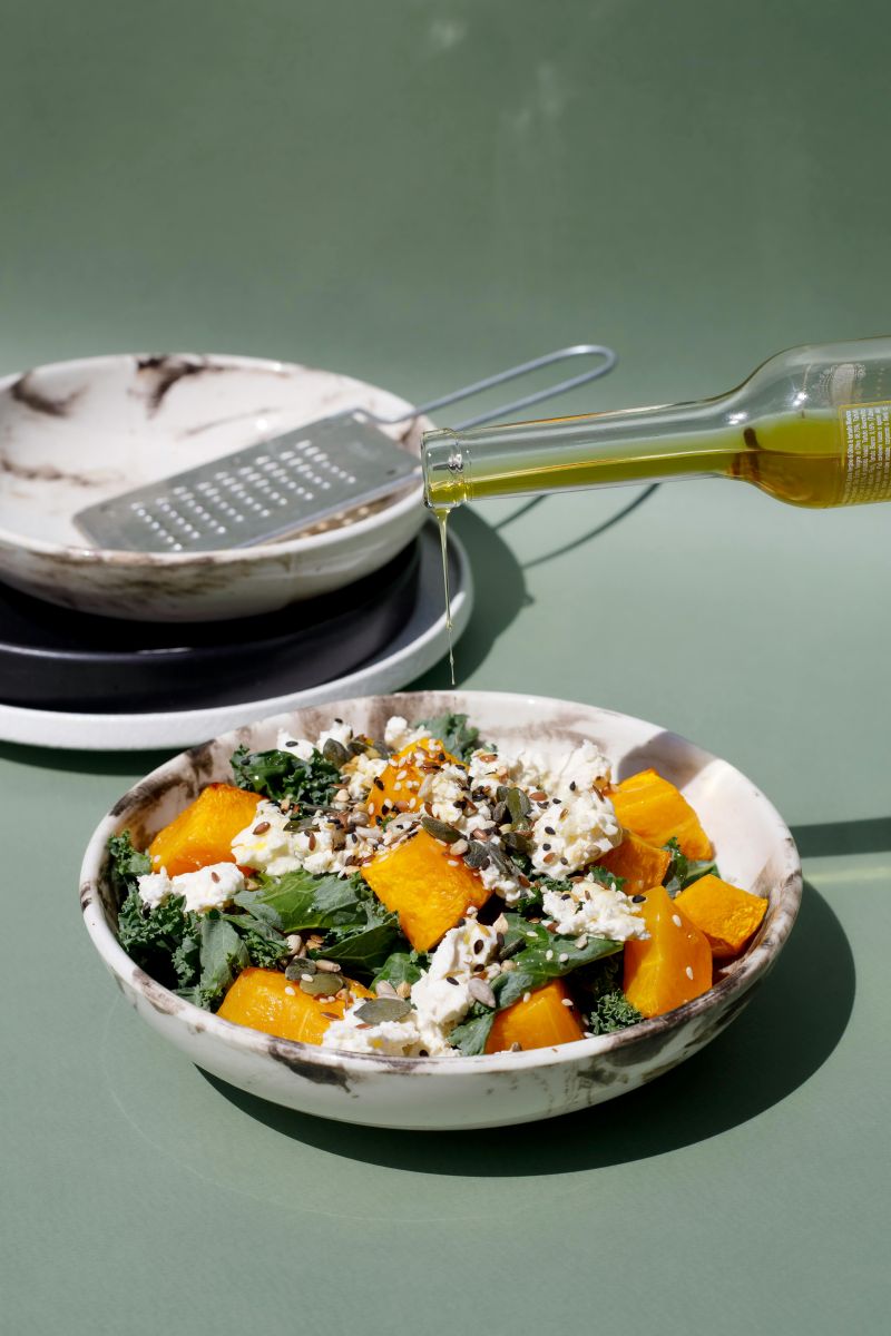 A delicious salad made with roasted pumpkin, kale, and crumbled feta cheese, topped with a mix of seeds and drizzled with olive oil.