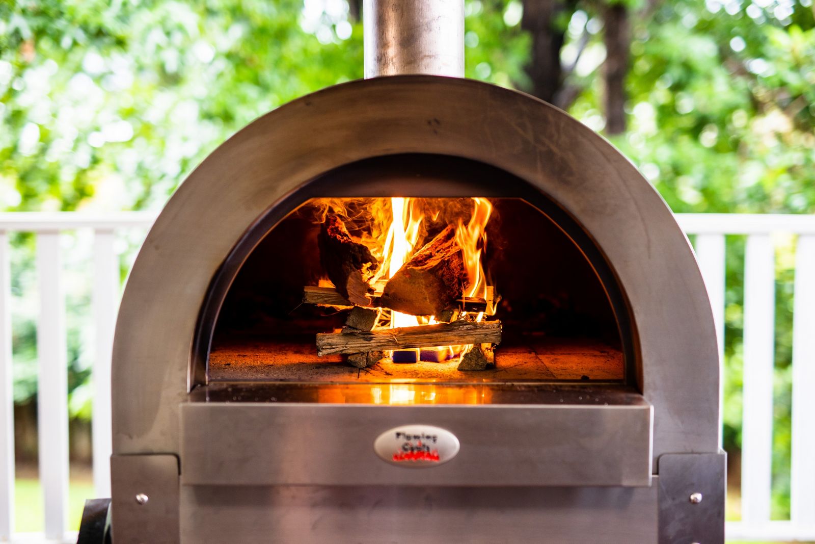 The image shows a Large Stainless Steel Woodfire Pizza Oven being used to cook pizzas