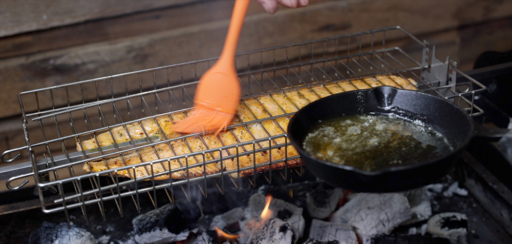 This image shows a salmon being basted with melted butter in a Spit Rotisserie