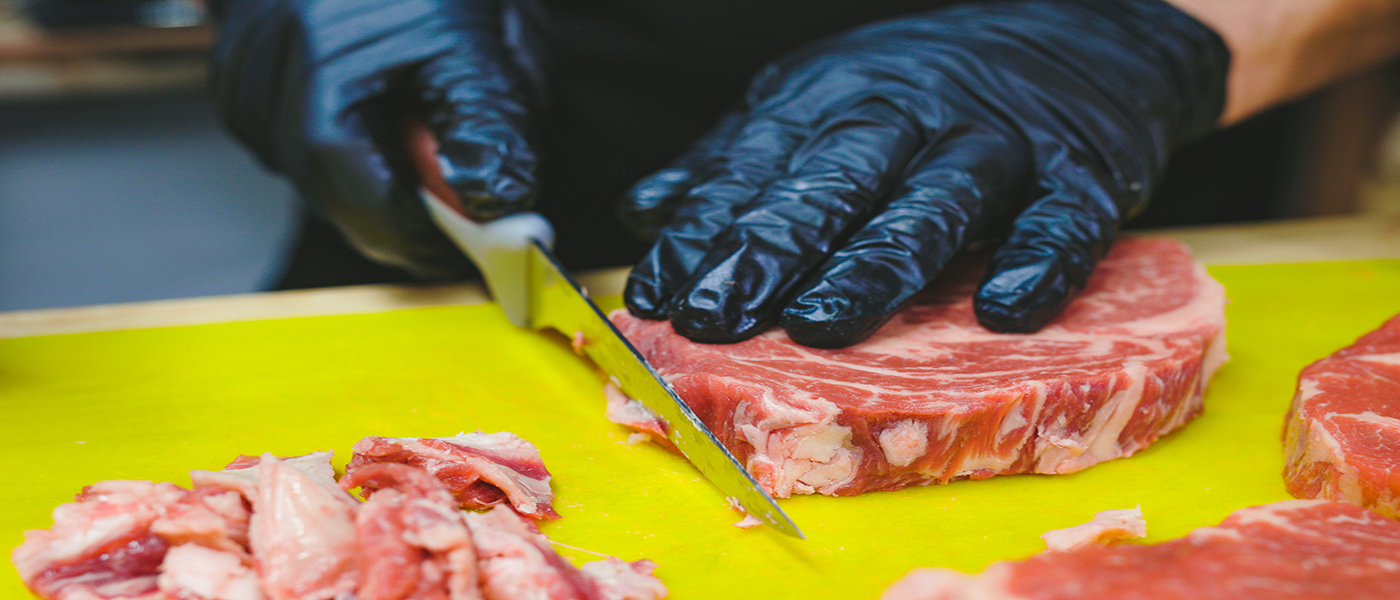 This image shows a man trimming the excess the fat of scotch fillet