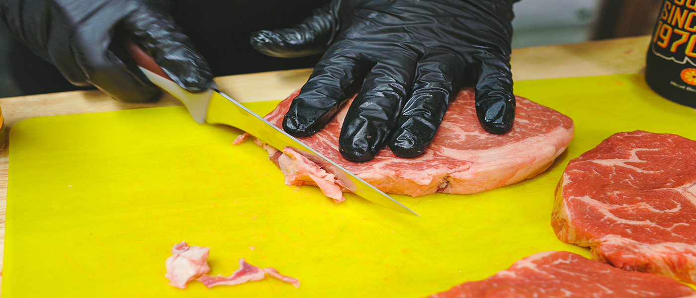 This image shows a man trimming the fat of Scotch Fillet