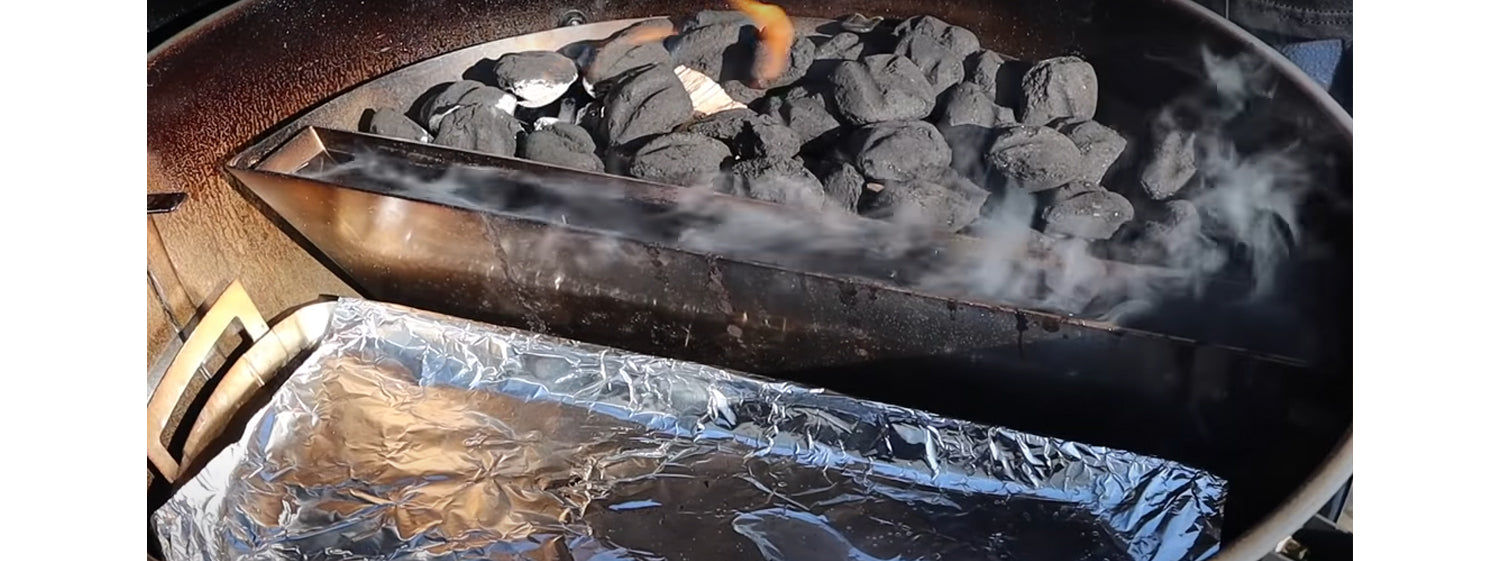 This image shows a Slow N Sear with lit charcoal and Drip and Roast Pan with foil