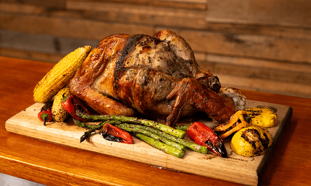 Whole spit-roasted turkey served on a wooden board with grilled vegetables including corn, asparagus, capsicum, and squash a festive Christmas roast presentation.