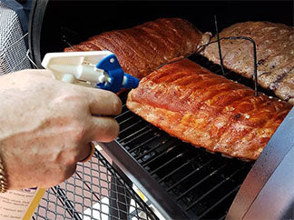 This image shows meat in a smoker being spritzed with apple cider vinegar. 