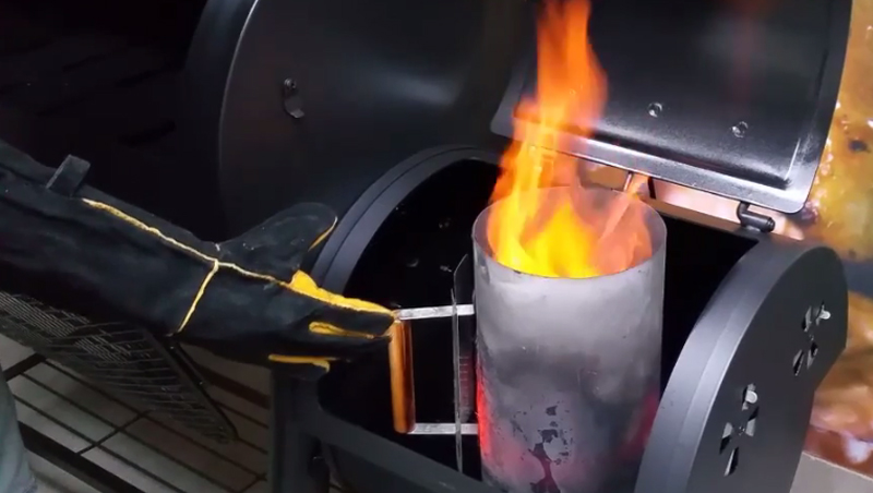 This picture shows a chimney starter full of coals being lit in an offset smoker. 