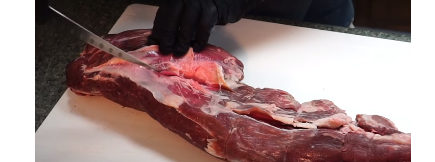 This image shows a man trimming the beef tenderloin. 