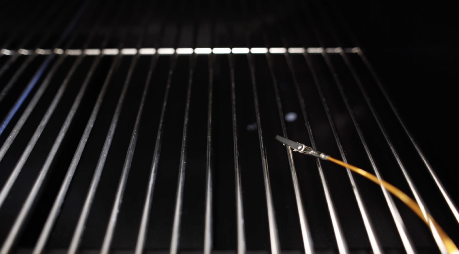 This image shows a wire of Tempmaster Pro clipped on the grill of smoker.