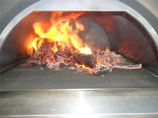 fire being lit in a wood fired pizza oven before cooking