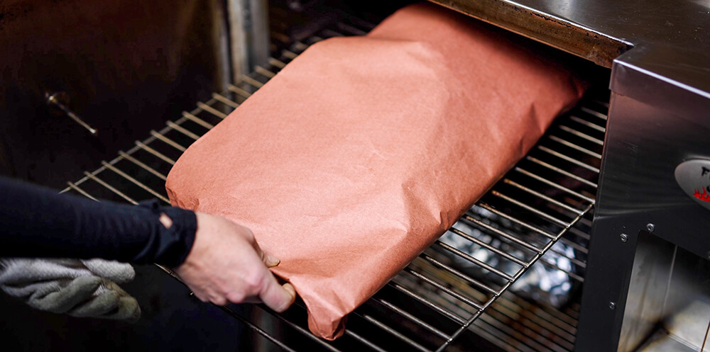 This image shows wrapped brisket being placed in the Flaming Coals Offset Smoker