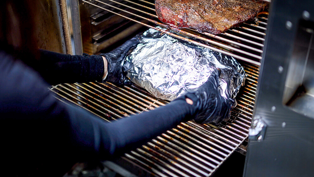 This image shows the wrapped pork being placed back in the Flaming Coals Offset Smoker